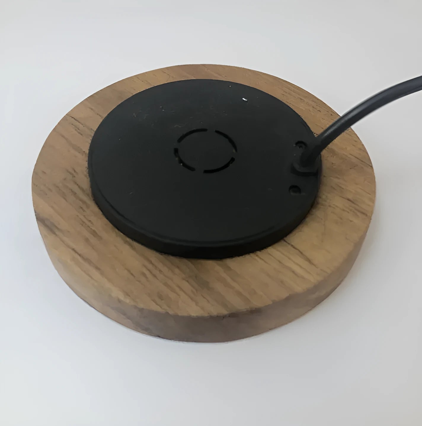 Round wireless charging unit for recessed installation in desks and tables, shown next to a smartphone.