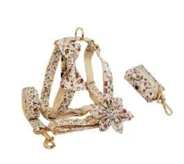 Small white flower patterned dog collar, leash, vest, bow, and poop bag holder set laid out flat.