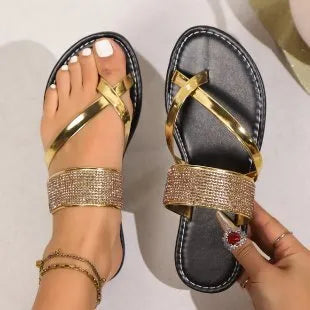 Women's flat beach sandals with a rhinestone-decorated toe strap in gold colour on a rubber sole.