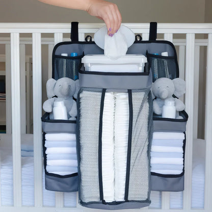 Grey baby nappy organiser attached to crib rail with Velcro straps, showing storage compartments for nappies and essentials