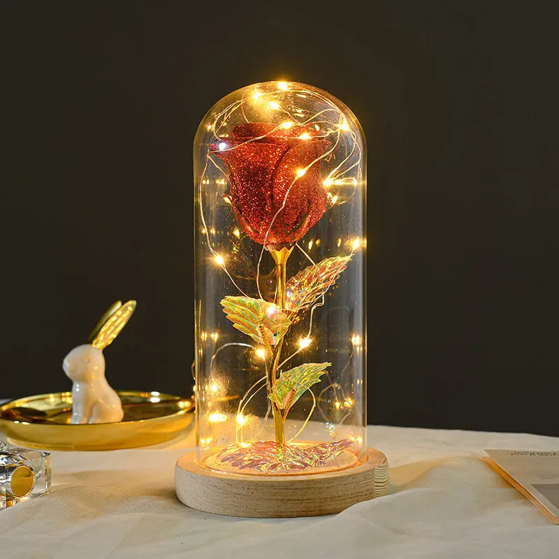 Red eternal rose flower arrangement with LED lights inside a glass dome on a table.