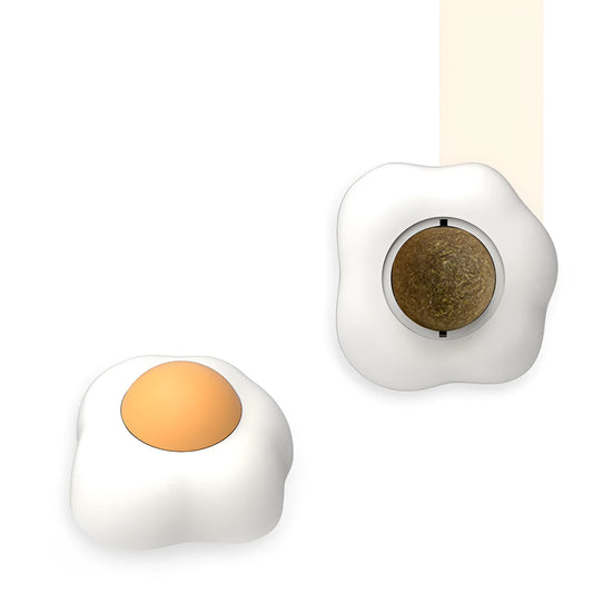 Interactive plush catnip ball toy shaped like a fried egg, stuck to a wall with a cat batting at it.