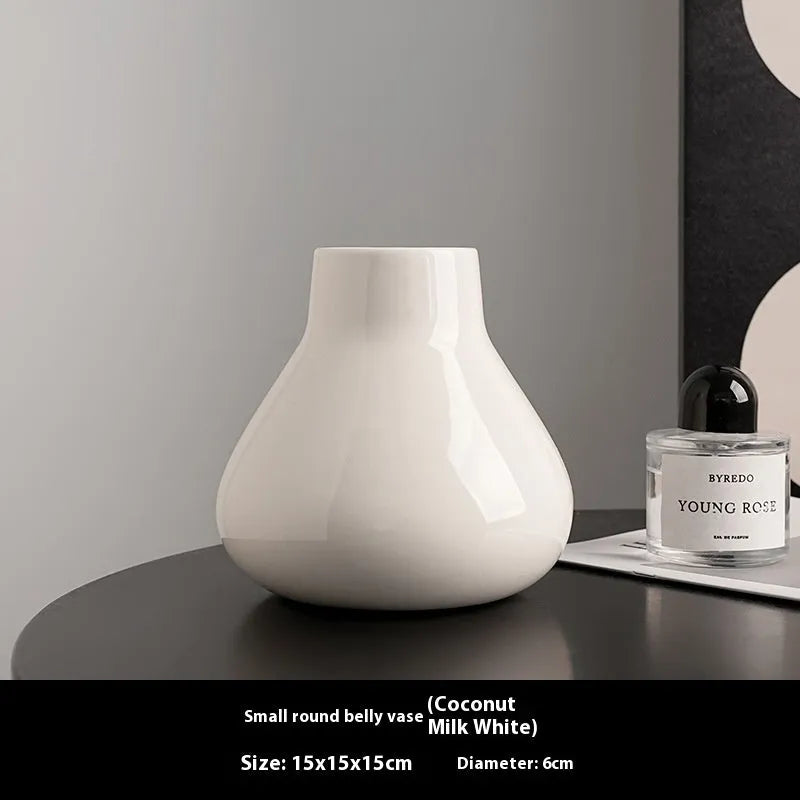 Black ceramic vase with round belly design and two white artificial orchid stems on wooden table