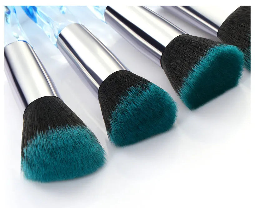 Ten clear crystal-handled foundation brushes with black synthetic bristles laid out on a surface.