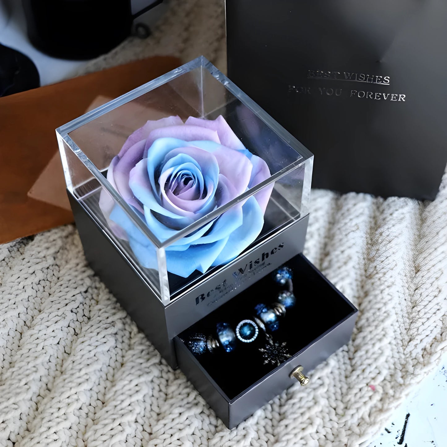 Blue and pink eternal flower gift box with roses and carnations on a table.
