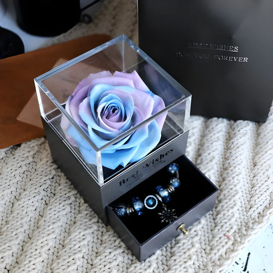 Blue and pink eternal flower gift box with roses and carnations on a table.