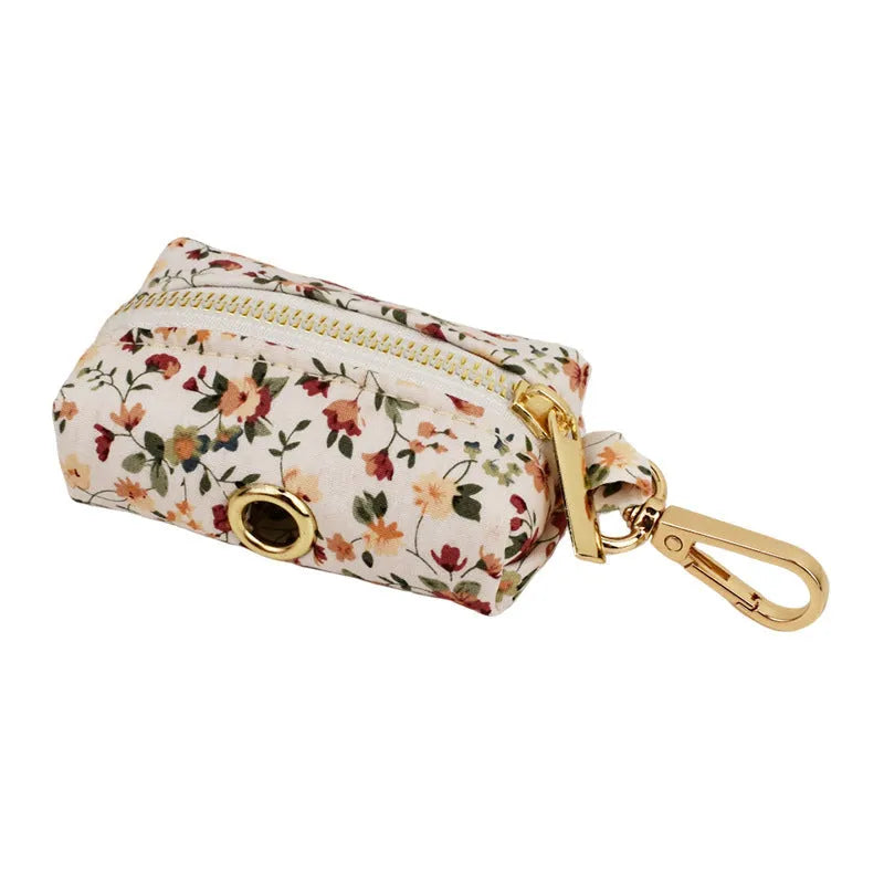 Small white flower patterned dog collar, leash, vest, bow, and poop bag holder set laid out flat.