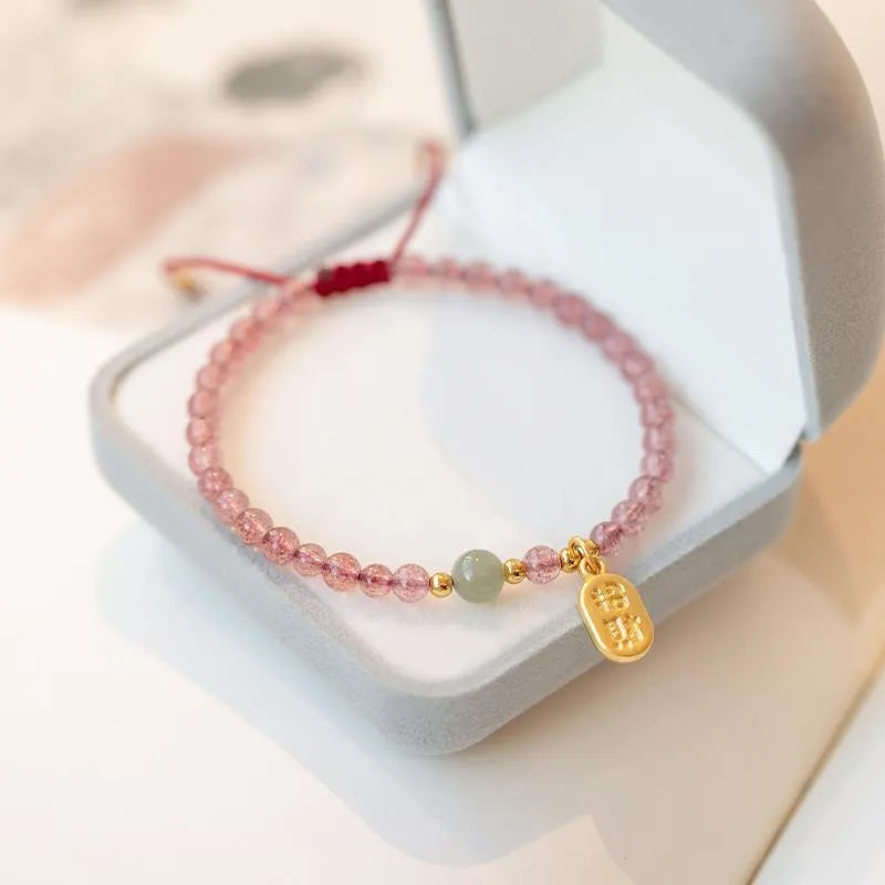 A hand-woven red rope bracelet with a strawberry quartz or garnet crystal, shown in simple styling.