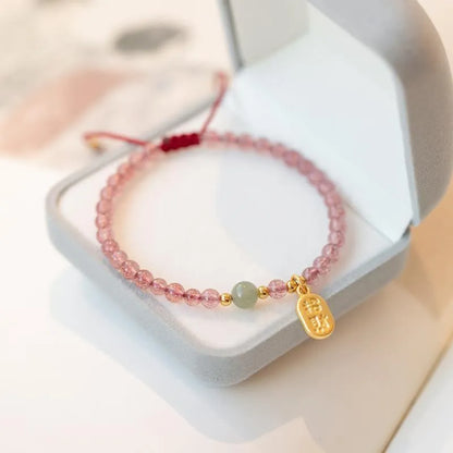 A hand-woven red rope bracelet with a strawberry quartz or garnet crystal, shown in simple styling.