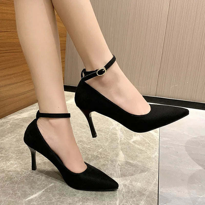 Women's black stiletto heels with skull pattern and ankle buckle closure on wooden floor