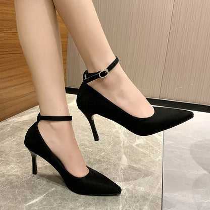 Women's black stiletto heels with skull pattern and ankle buckle closure on wooden floor