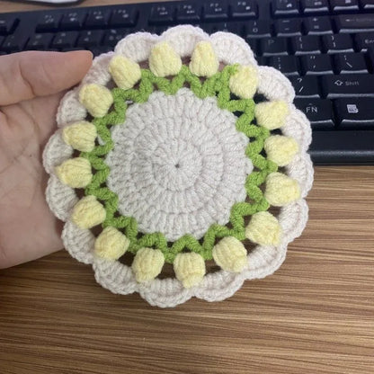 Handmade woven flower coaster in cotton and linen on a wooden table.