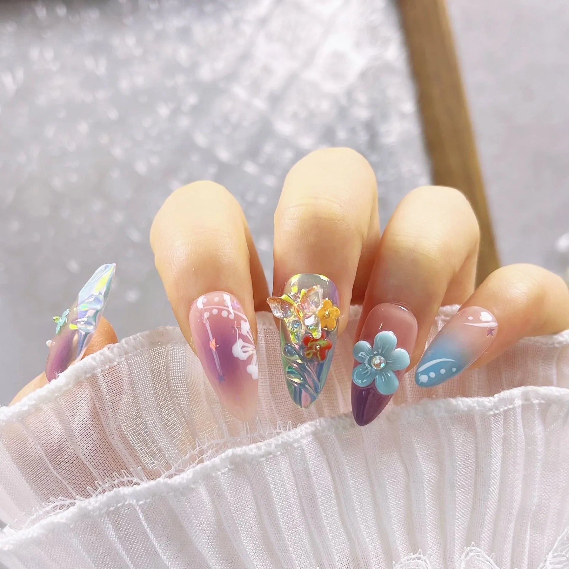 Handmade 3D sculpted butterfly and embossed flower nail art decorations in four sizes on a manicure.