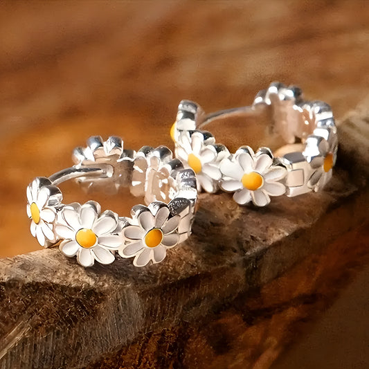 A pair of white daisy flower ring earrings with an inlaid gemstone in a platinum setting.