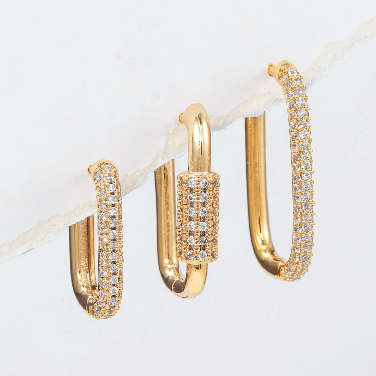 Three geometric copper ear clips with micro inlaid zircon in gold and white tones on a grey background.