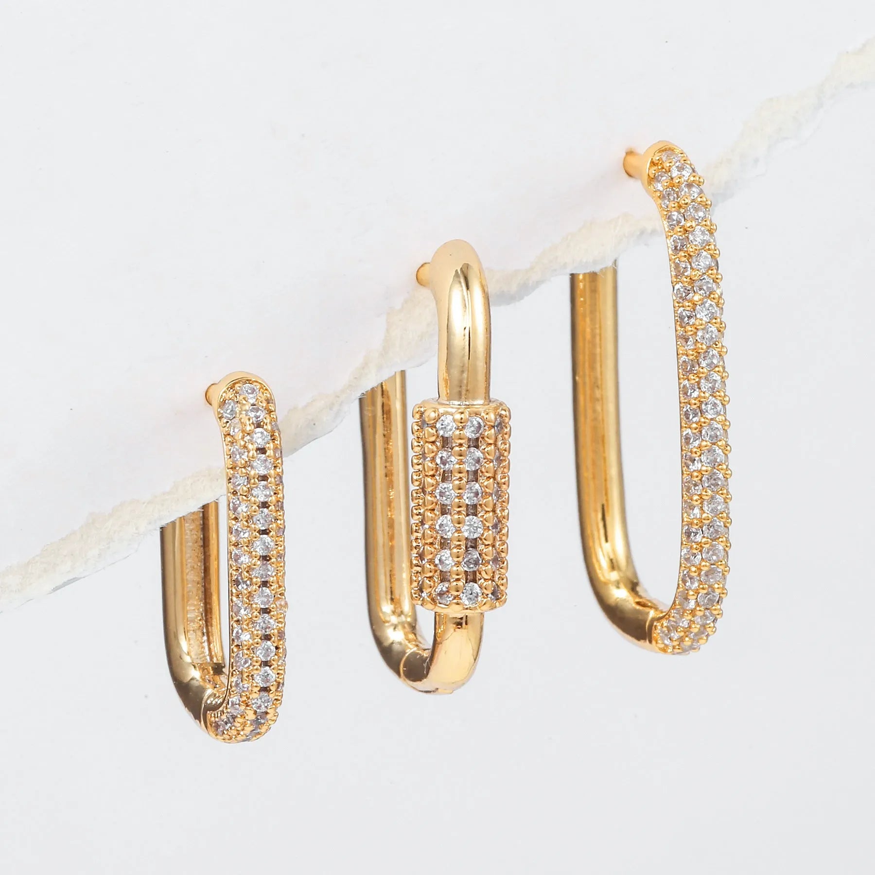 Three geometric copper ear clips with micro inlaid zircon in gold and white tones on a grey background.