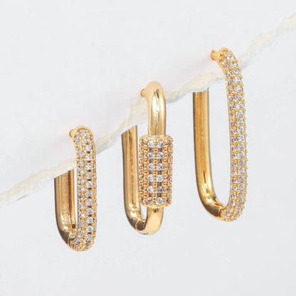 Three geometric copper ear clips with micro inlaid zircon in gold and white tones on a grey background.