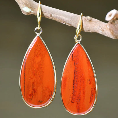 Close-up of long, polished tigereye stone drop earrings with a fishhook clasp on a neutral background.