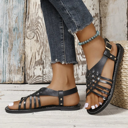Black Roman style beach slippers with cross straps and buckle fastening on wooden floor