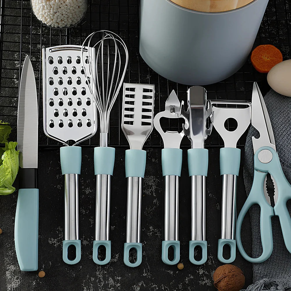 Stainless steel kitchen utensil set with whisk, grater, peeler, scissors and other tools on grey background