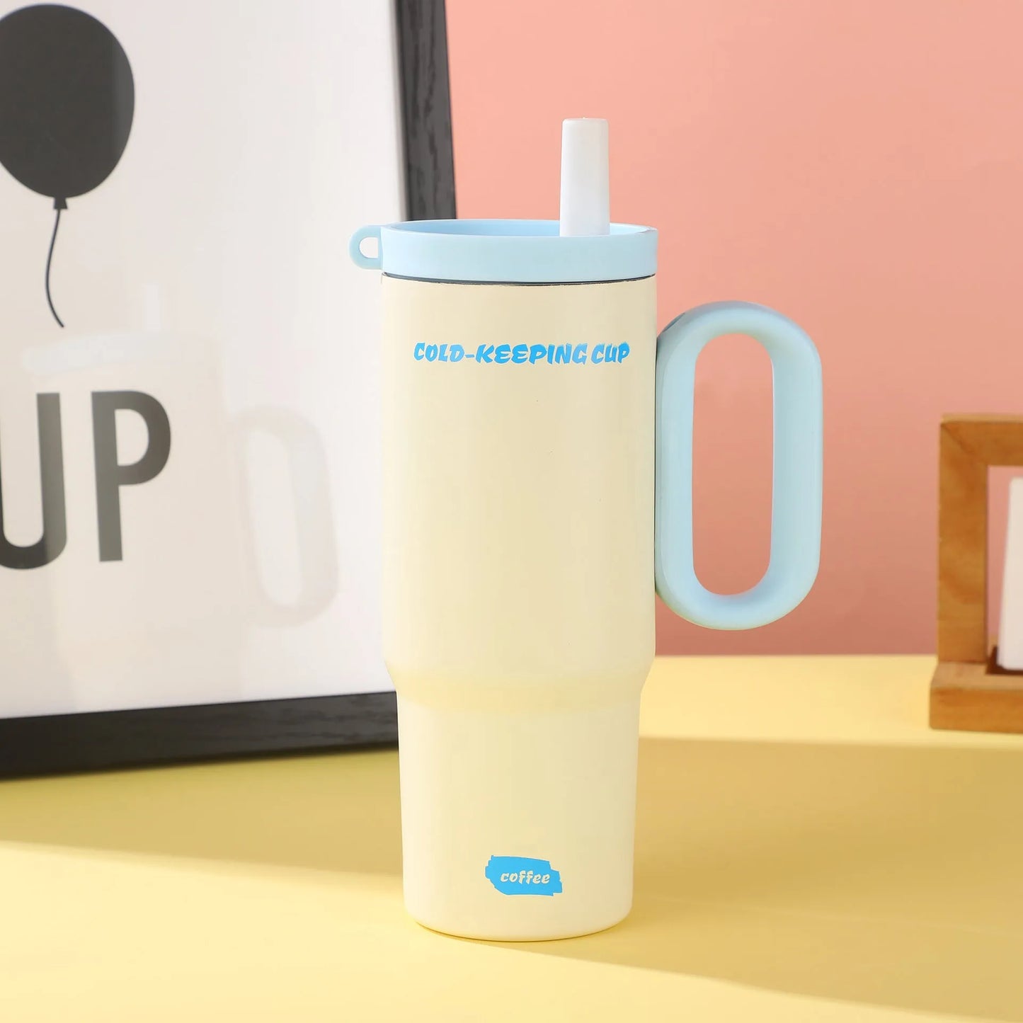 Large pink insulated straw cup with a black handle and push-button lid on a wooden table