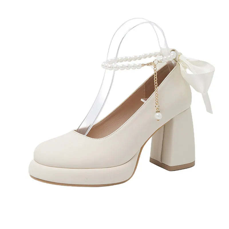 Women's beige Mary Jane shoes with chunky heel, ankle strap, pearl buckle, and round toe on a rubber sole.