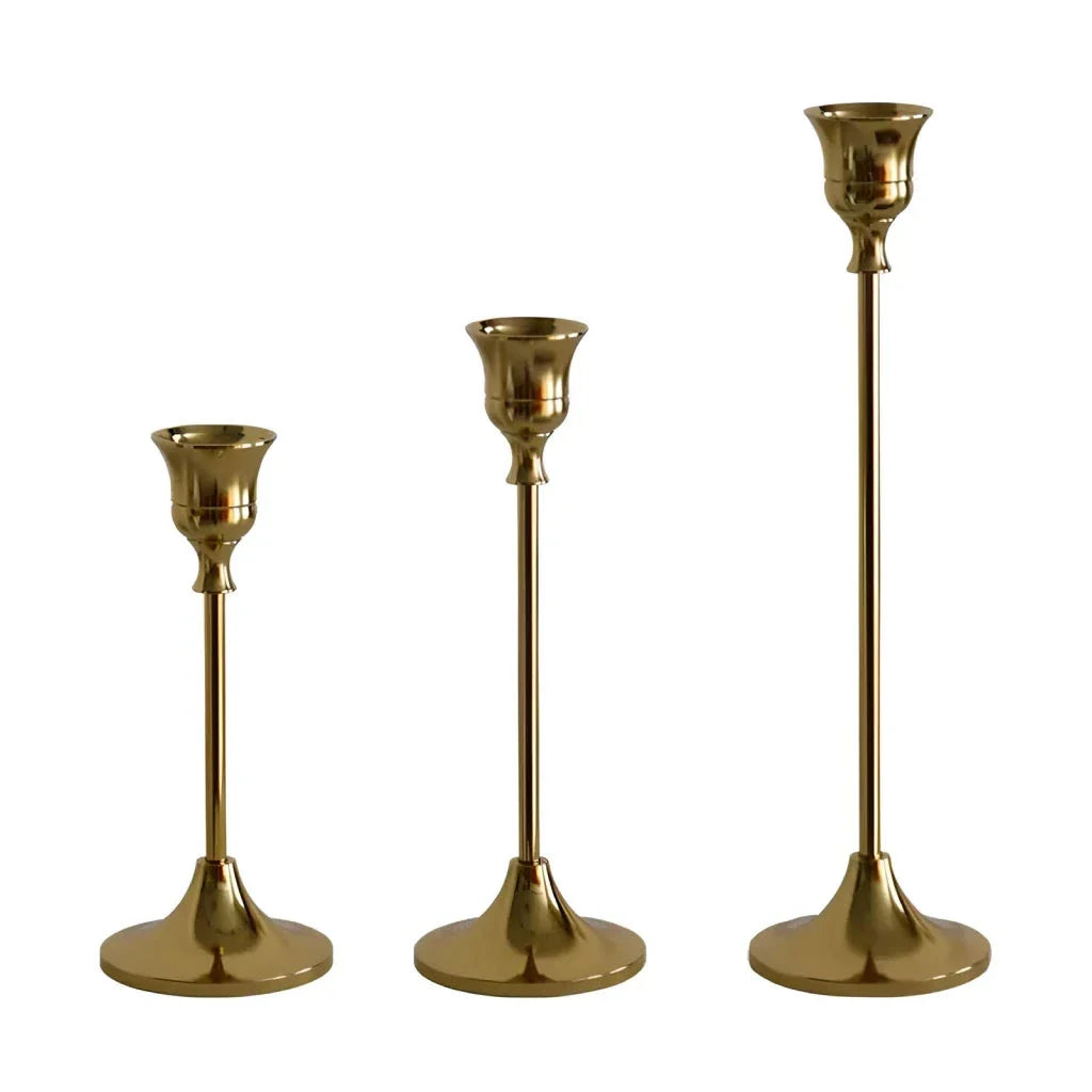 A set of three elegant brass gold candlestick holders on a wooden surface, creating a warm and inviting ambiance.