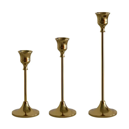 A set of three elegant brass gold candlestick holders on a wooden surface, creating a warm and inviting ambiance.