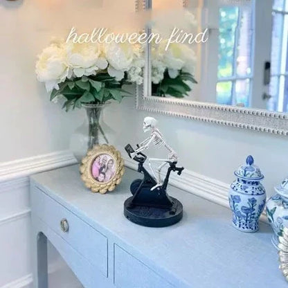 Animated skeleton cycling ornament in white, with the skeleton gracefully pedaling a tiny bicycle