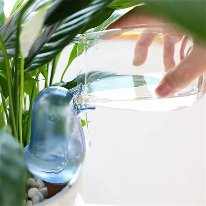 Automatic bird-shaped plant waterer in blue and red colors, designed to keep plants hydrated with a transparent design and slow-release watering mechanism.