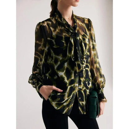 A silk blend blouse with a camouflage print and a bow collar, designed for versatile wear.