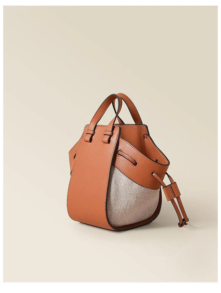 A stylish drawstring bucket bag made from premium cowhide leather and canvas, featuring a spacious main compartment, adjustable shoulder strap, and a softly structured design.
