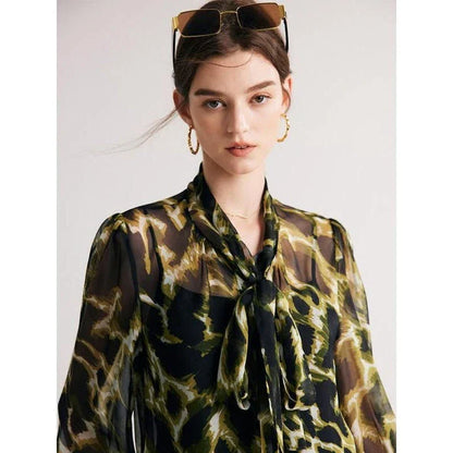 A silk blend blouse with a camouflage print and a bow collar, designed for versatile wear.