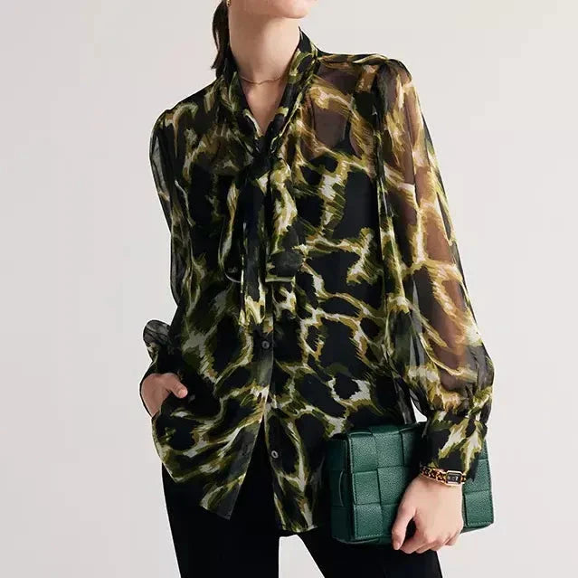 A silk blend blouse with a camouflage print and a bow collar, designed for versatile wear.