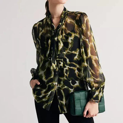 A silk blend blouse with a camouflage print and a bow collar, designed for versatile wear.
