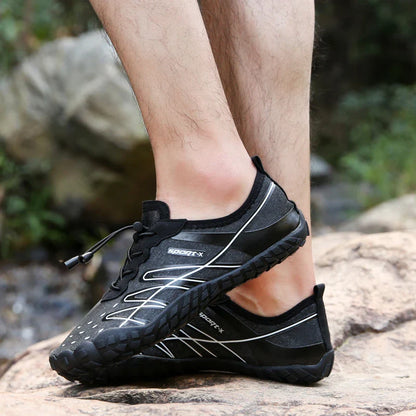 Couple wearing blue, black, and khaki five-finger water shoes, wading in a stream and exploring a rocky beach