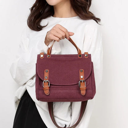 A stylish women's canvas crossbody handbag in an orange color, featuring a small square shape and a horizontal design.