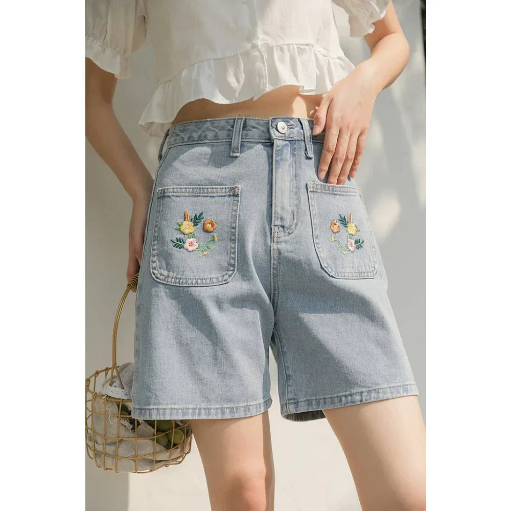 Light blue denim shorts with delicate floral embroidery, providing a stylish and comfortable summer look for women.