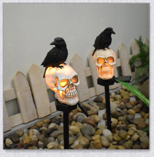 A solar-powered landscape light in the shape of a crow perched on a skull, providing an eerie and captivating outdoor decoration.