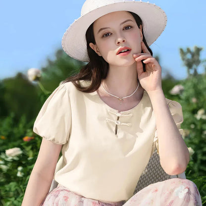 Woman wearing a chic, plated puff short-sleeve summer top in a cream apricot color
