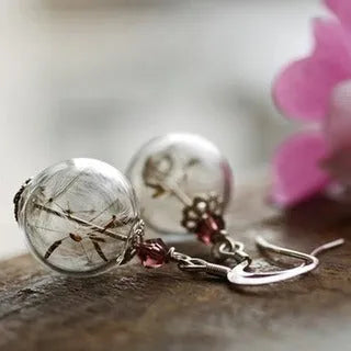 Close-up of a transparent 16mm glass ball earring with a dandelion seed inside, on a silver French hook.