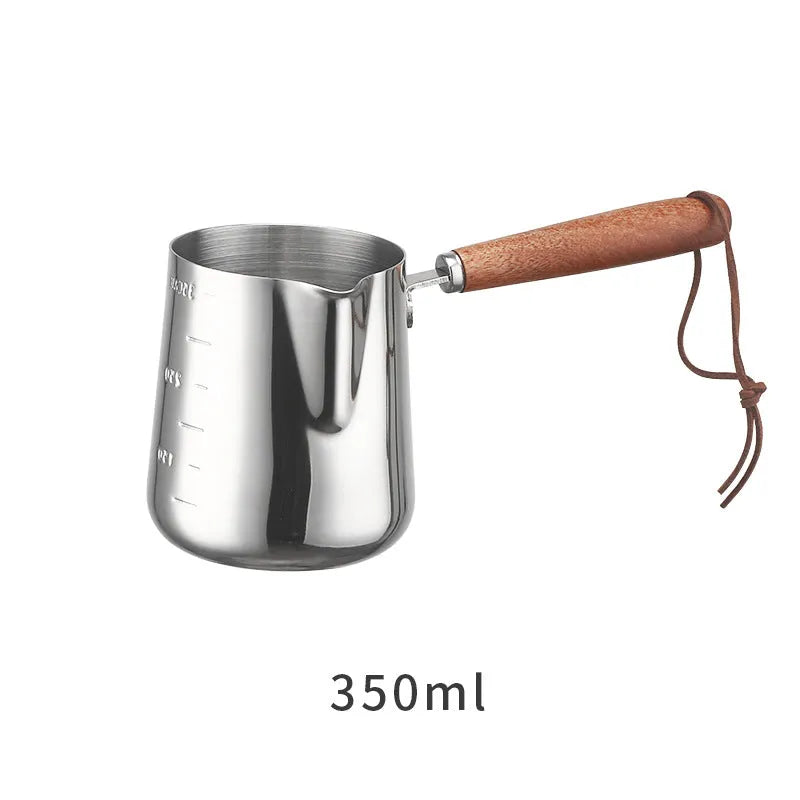 Stainless steel barista milk jug with wooden handle and internal measurement scale for latte art.