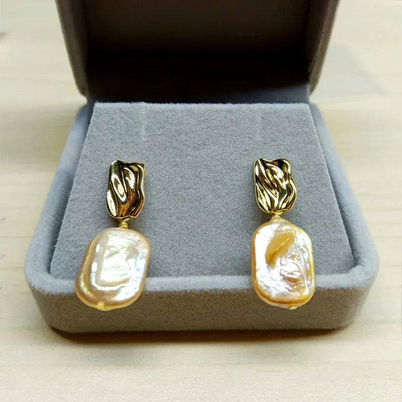 A pair of square stud earrings with a natural freshwater pearl in a geometric alloy setting.