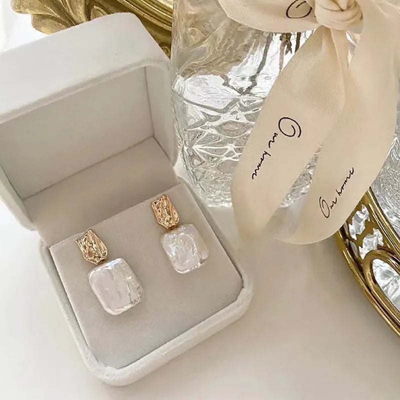 A pair of square stud earrings with a natural freshwater pearl in a geometric alloy setting.