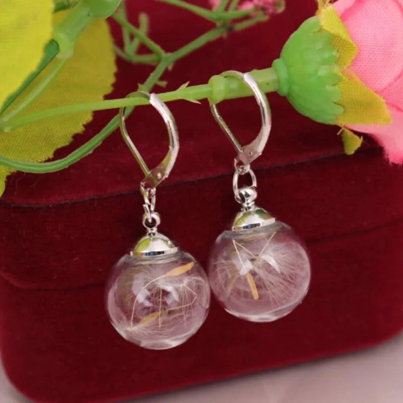 Close-up of a transparent 16mm glass ball earring with a dandelion seed inside, on a silver French hook.