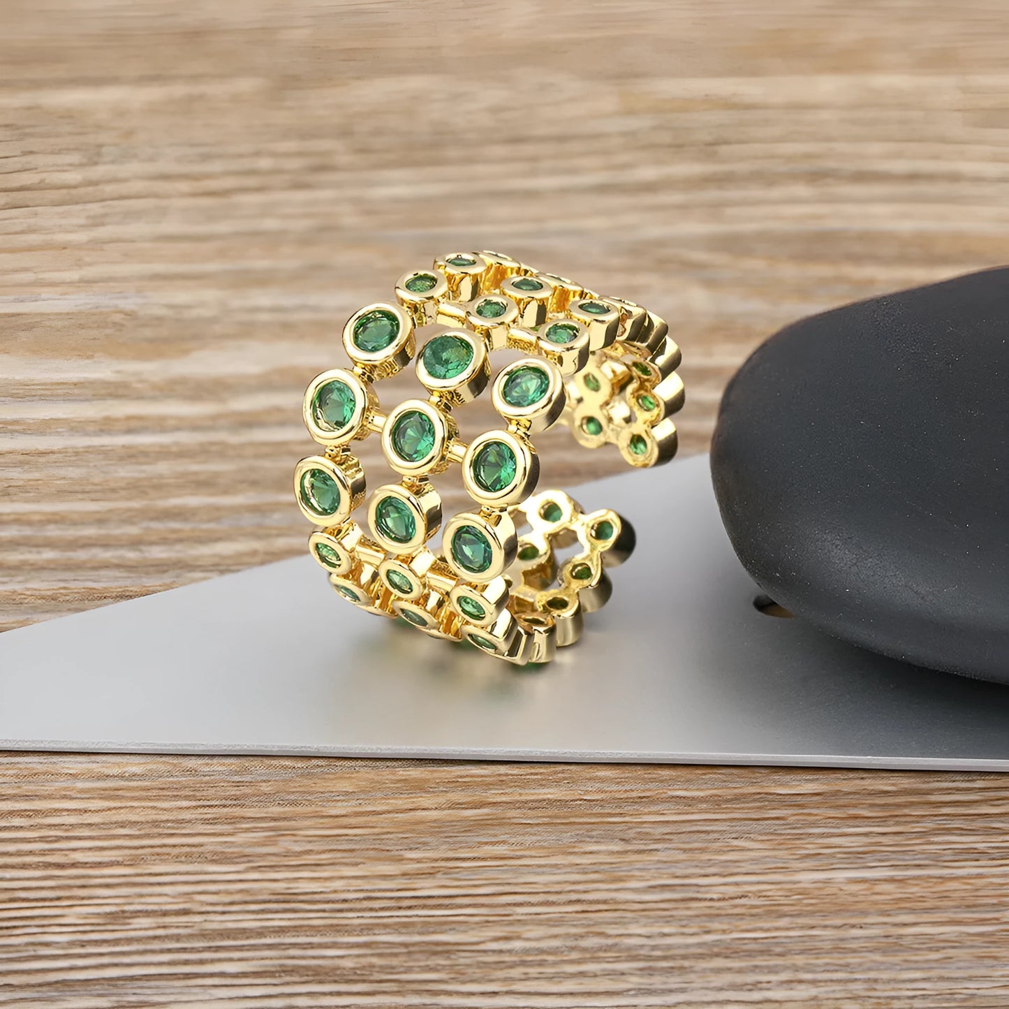 Wide gold plated copper ring with a full band of sparkling green cubic zirconia stones on a hand.