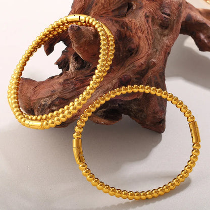 Stainless steel open-end bracelet with a buckle clasp in a gold electroplated finish featuring circle design elements.