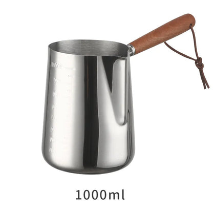 Stainless steel barista milk jug with wooden handle and internal measurement scale for latte art.