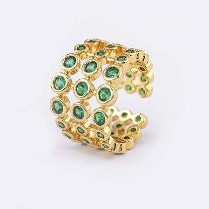 Wide gold plated copper ring with a full band of sparkling green cubic zirconia stones on a hand.