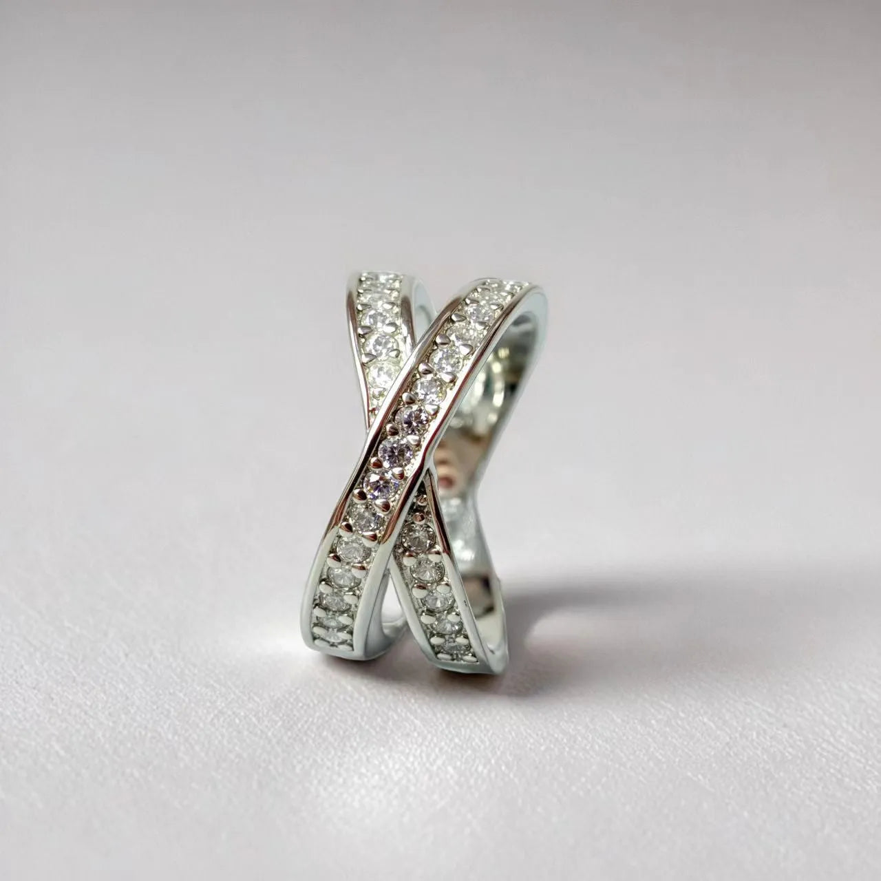 Silver geometric cross ring with micro-inlaid zircon stones on finger, showing simple design with heart-shaped elements